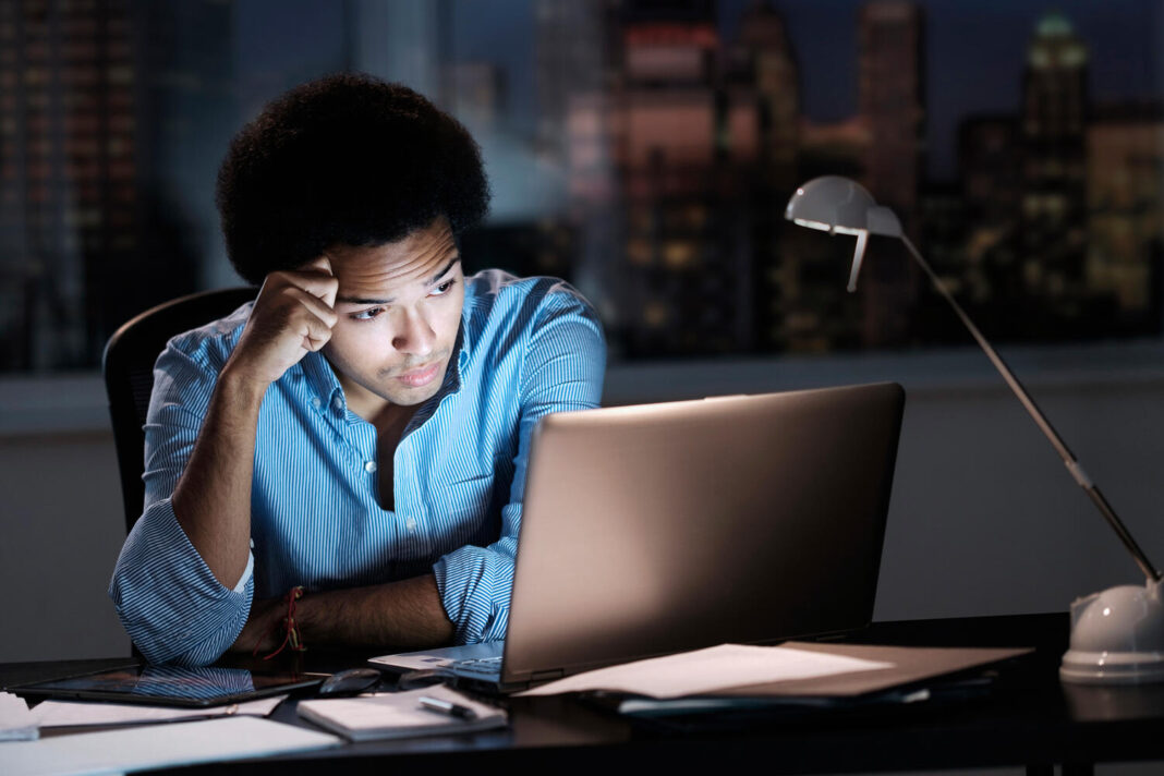 Mixed race businessman wearing blue shirt working late in dark office
